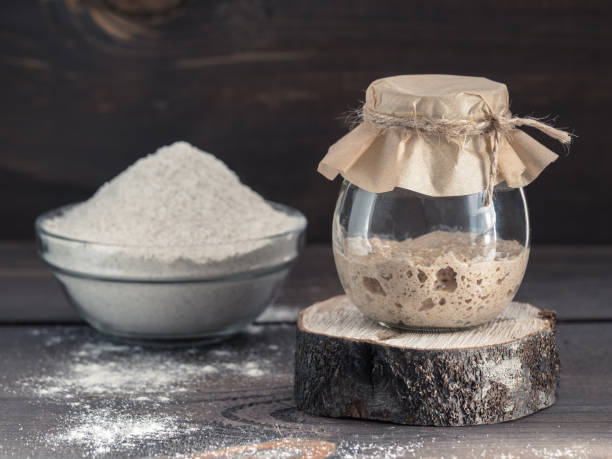 rye sourdough starter and rye flour Active rye sourdough starter in glass jar and rye flour on brown wooden background. Starter for sourdough bread. Toned image. Copy space. yeast stock pictures, royalty-free photos & images