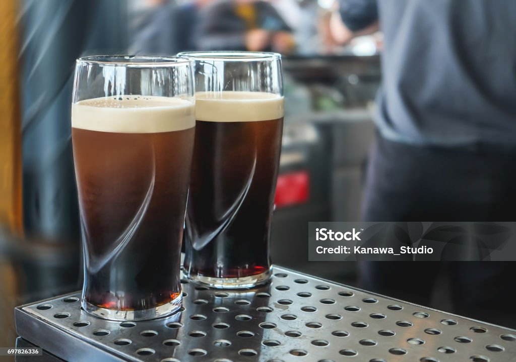 Two pint of  dark beer on the bar Close up two pints of dark beer above stainless steel bar counter, ready to drink. Pint Glass Stock Photo