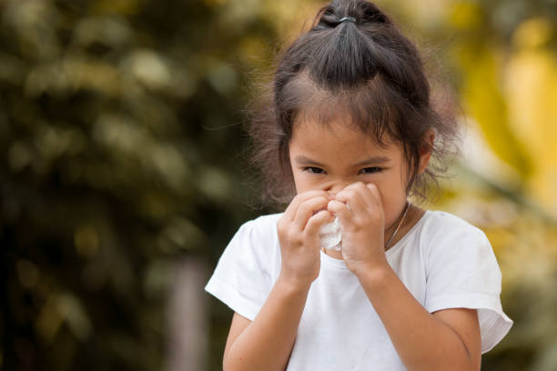 Sick little asian girl wiping or cleaning nose with tissue on her hand stock photo