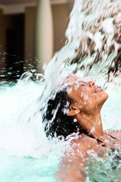 istock Young woman is drenched by a pool's artificial waterfall 697860486