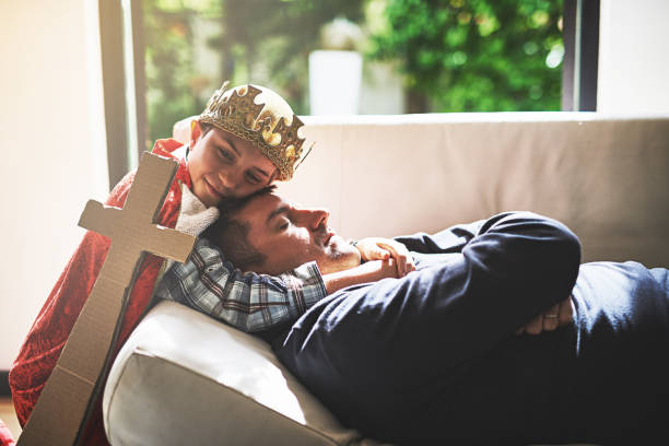 Sweet dreams, daddy Shot of a little boy in a king's costume hugging his sleeping father on the couch prince royal person stock pictures, royalty-free photos & images