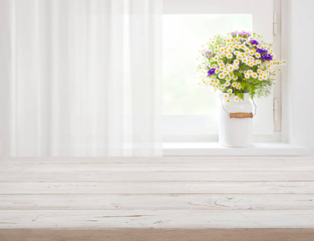 istock Wooden rustic table in front of wild flowers on windowsill 697868222