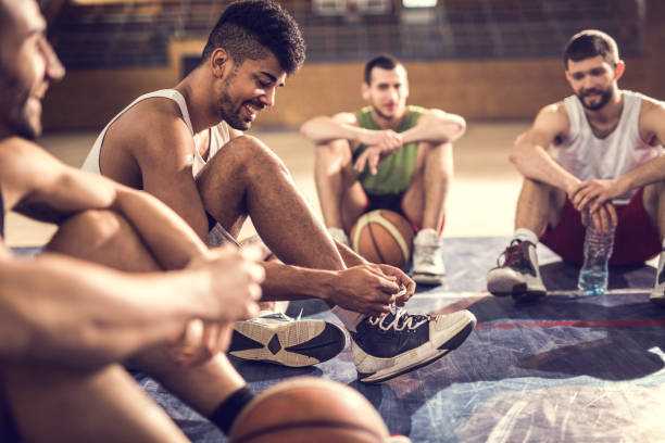 Happy African American basketball player tying shoelace while relaxing on basketball court with friends.