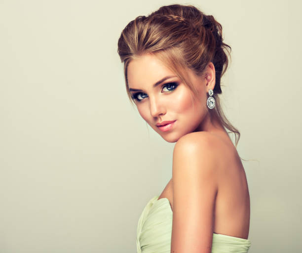 Young and attractive blond model dressed in evening gown and openwork earings. Beautiful woman dressed in evening gown. Example of wedding hairstyle for blond-haired ladies. Young and attractive blond model, straight look on camera. Trendy hairstyles, make up and outfit. hairstyle bride jewelry women stock pictures, royalty-free photos & images