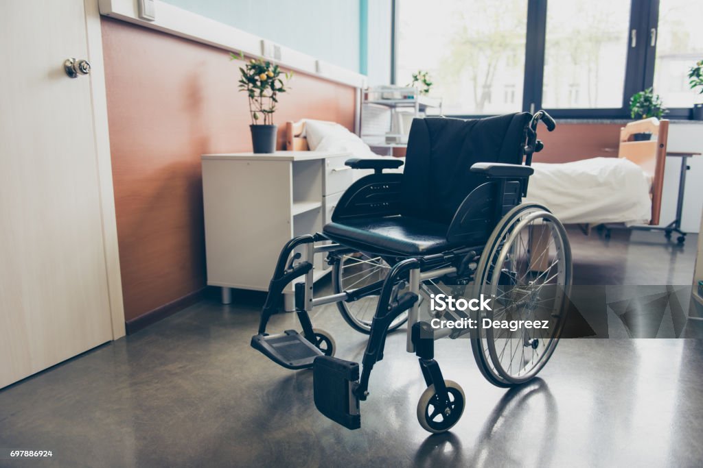 Silla de ruedas negro aislada en la sala vacía del hospital - Foto de stock de Silla de ruedas libre de derechos