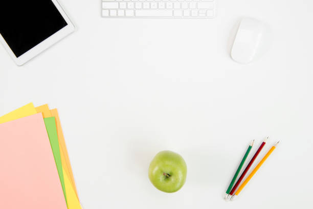 istock Top view of keyboard, computer mouse, digital tablet with blank screen, green apple and office supplies at workplace 697887146