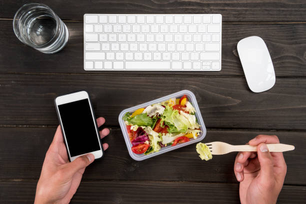 istock Top view of human hand eating fresh salad and using smartphone during work. 697888030