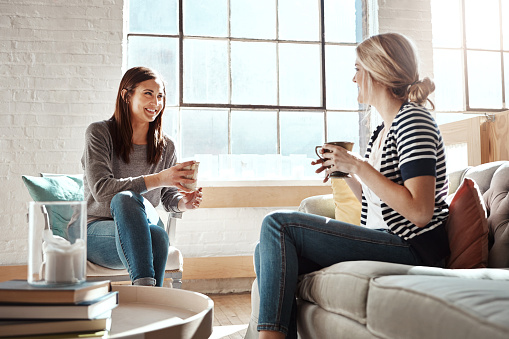 Shot of two women having coffee and chatting while sitting in a living room