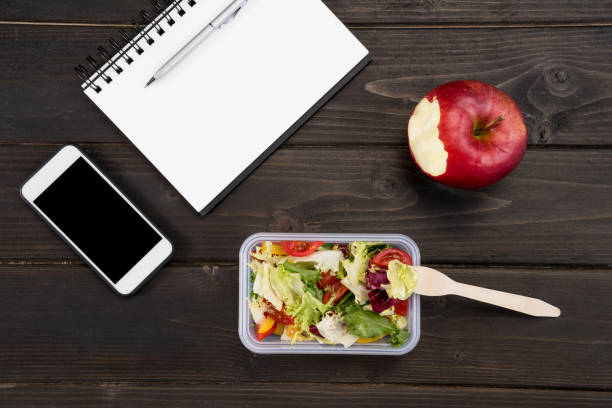 Top view of organic salad with apple, notebook and smartphone on wooden table Top view of organic salad with apple, notebook and smartphone on wooden table apple with bite out of it stock pictures, royalty-free photos & images