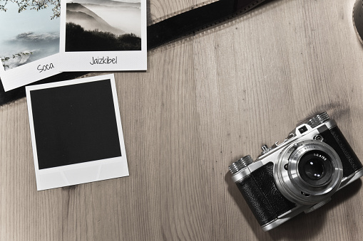 Retro vintage photography concept of three instant photo frames cards on wooden background with images of nature and text and blank black photo frame with old camera and film strip top view