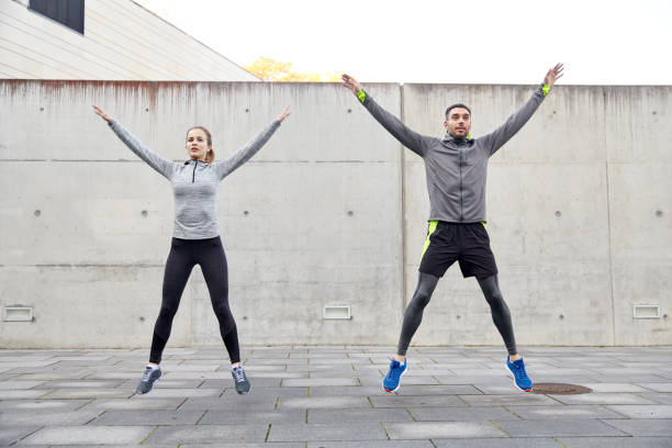 happy man and woman jumping outdoors fitness, sport, people, exercising and lifestyle concept - happy man and woman doing jumping jack or star jump exercise outdoors JUMPING JACKS stock pictures, royalty-free photos & images