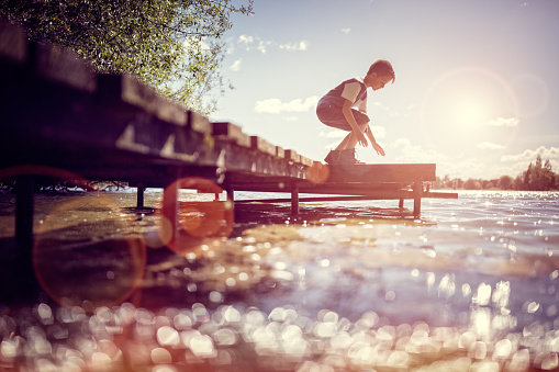 Boy playing on a pier by lake on summer holiday vacation