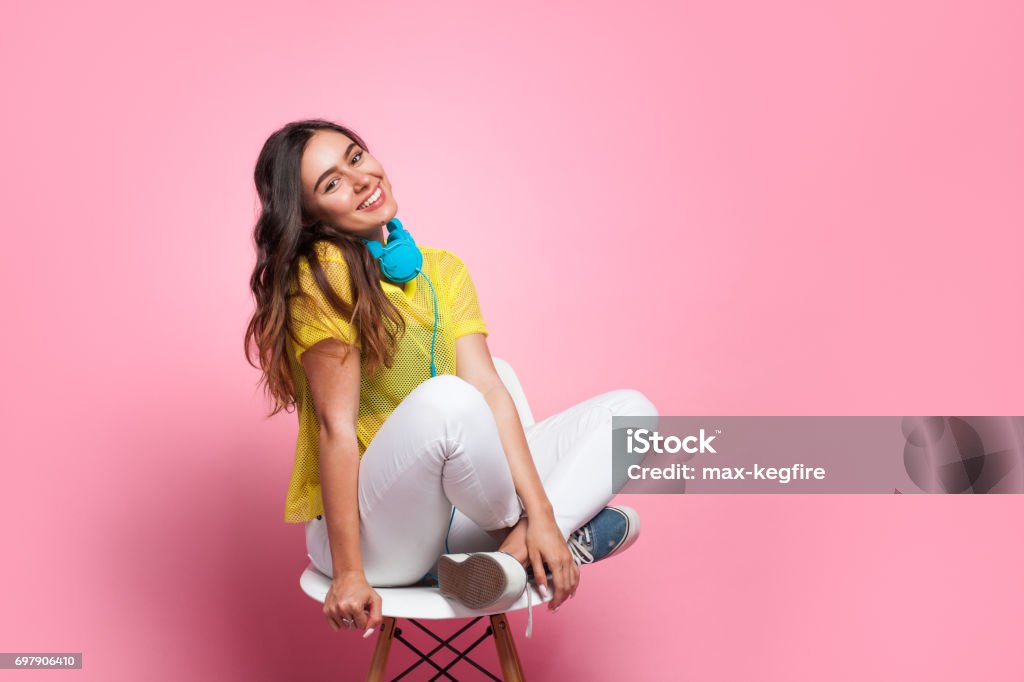 Young teenager on chair Smiling girl with in casual clothing sitting on chair with big blue headphones. Teenager Stock Photo
