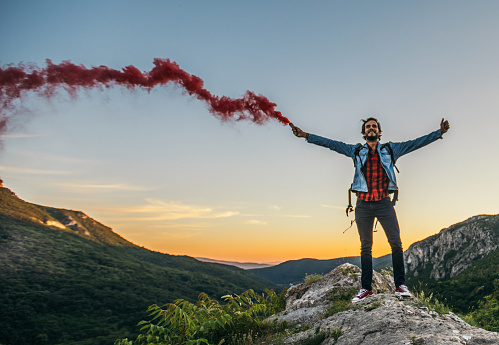 Young handsome hiker with open arm holds a singnal smoke flare