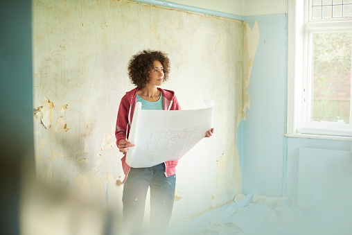 a young woman  takes time out from scraping walls in their new house to visualise on their digital tablet
