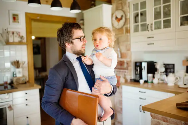 Photo of Businessman coming home, holding little son in the arms.