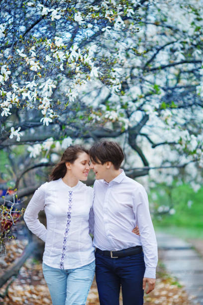 uomo e donna si abbracciano in giardino con magnolie in fiore - tree harmony couple trust foto e immagini stock