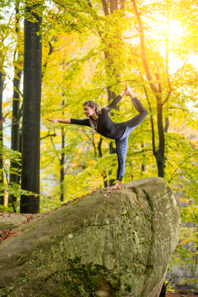 istock Woman is practicing yoga in autumn forest on the big stone 697928534