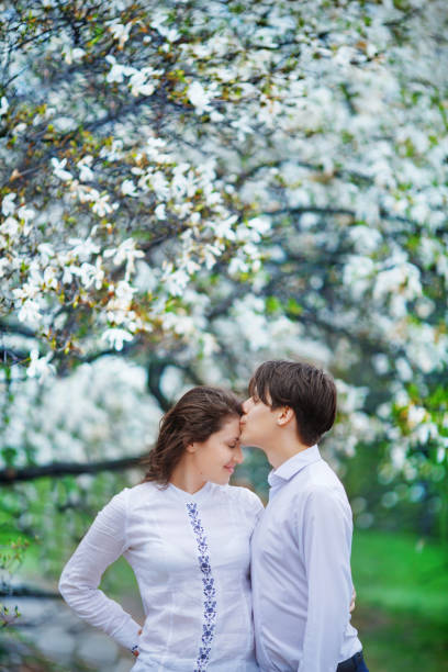 l'uomo bacia delicatamente la fronte della donna in giardino con magnolie in fiore - tree harmony couple trust foto e immagini stock