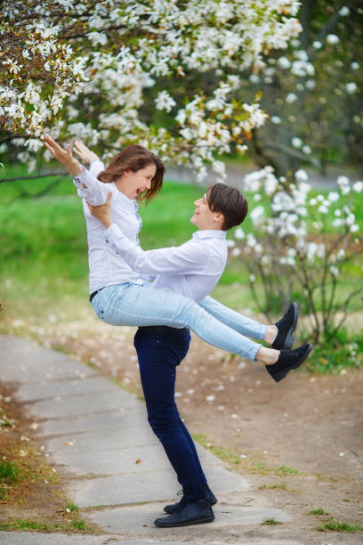 l'uomo tiene una donna in giardino con magnolie in fiore - tree harmony couple trust foto e immagini stock