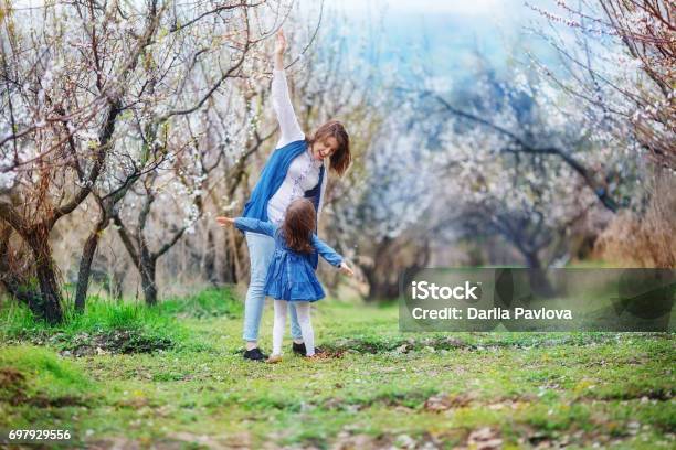 Mom And Daughter Mimic The Wings Of An Airplane Standing In The Midst Of A Flowering Apricot Garden Stock Photo - Download Image Now