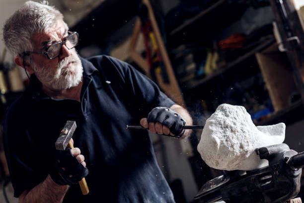 Senior sculptor working on his marble sculpture in his workshop with grinder.