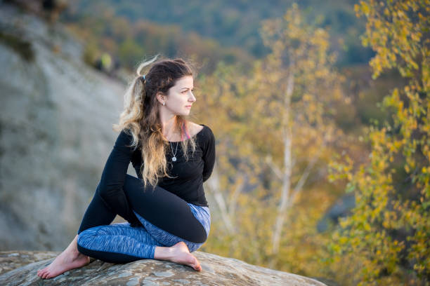 Sporty fit woman is practicing yoga on the top of the mountain Attractive female is practicing yoga and doing asana Arha Matsyendrasana on the top of the high rocky mountain. Autumn forests, rocks and hills on the background arhanes stock pictures, royalty-free photos & images