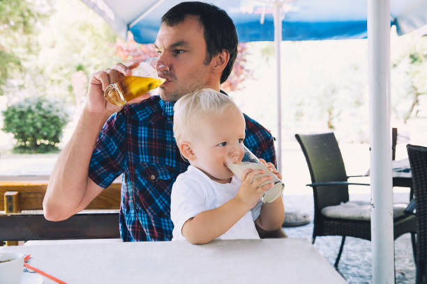 padre toma cerveza, niño bebe zumo en un bar de playa. - los niños y los padres brindis bebidas mientras almuerza fotografías e imágenes de stock