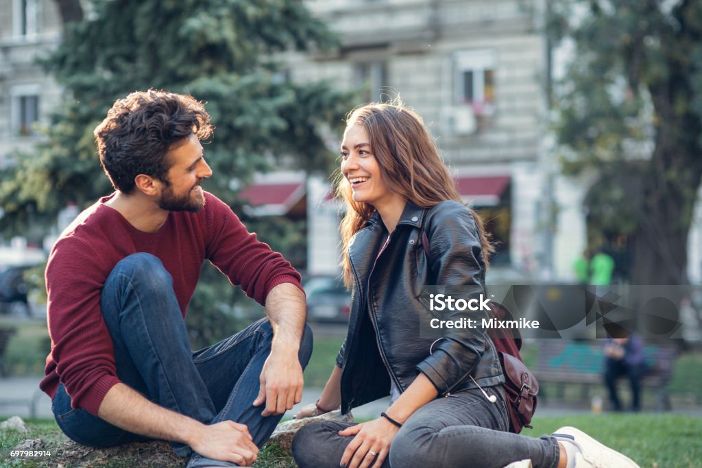 Couple on a date at the park Happy couple talking while sitting on a meadow Dating Stock Photo