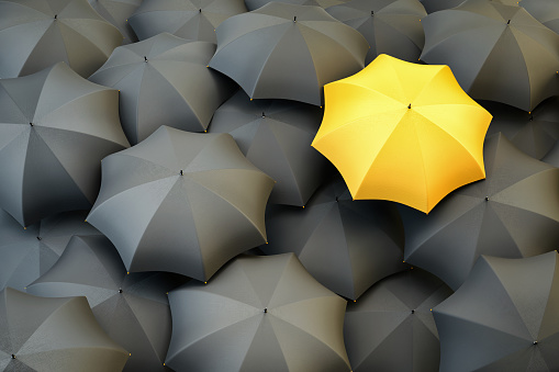 Top view of unique yellow umbrella standing out from the gray crowd