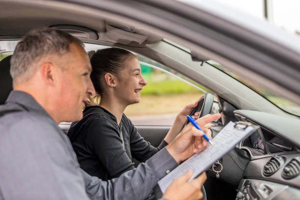 Driving Test, Focused on the road ahead of her Driving male instructor  taking notes while holding clipboard while sitting next to driving female teen student learning to drive during bright suuny day. driving test photos stock pictures, royalty-free photos & images