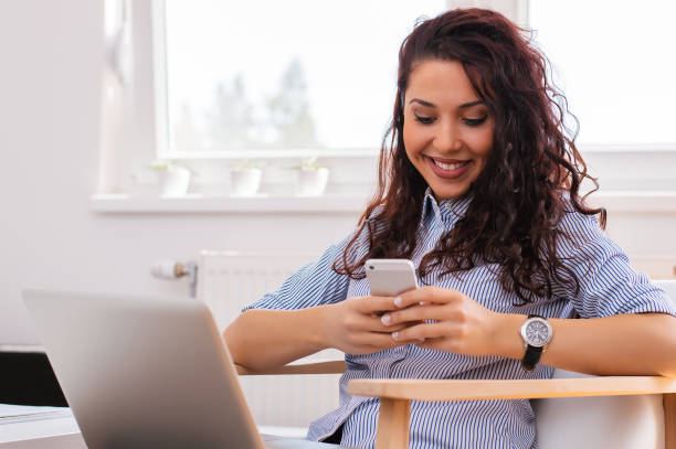 istock Pretty girl using her phone while sitting next to lap top 698005098