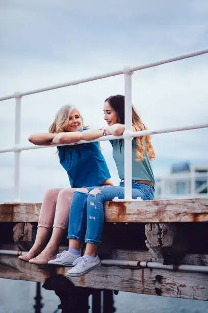 Photo of Grandmother and teenage granddaughter having fun sitting on a jetty