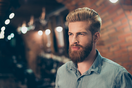 Close up of a stunning look of a red bearded guy with trendy hairdo in a barber shop. Looking so fashionable and confident