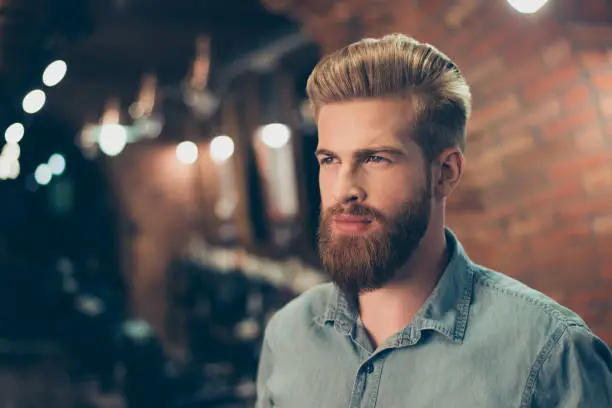 Photo of Close up of a stunning look of a red bearded guy with trendy hairdo in a barber shop. Looking so fashionable and confident