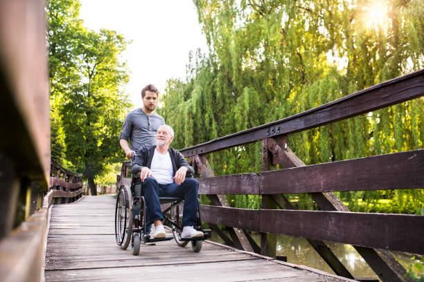 istock Hipster son walking with disabled father in wheelchair at park. 698034982