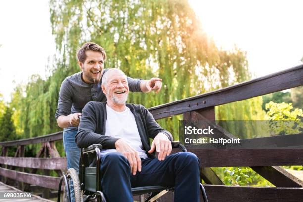 Hipster Son Walking With Disabled Father In Wheelchair At Park Stock Photo - Download Image Now