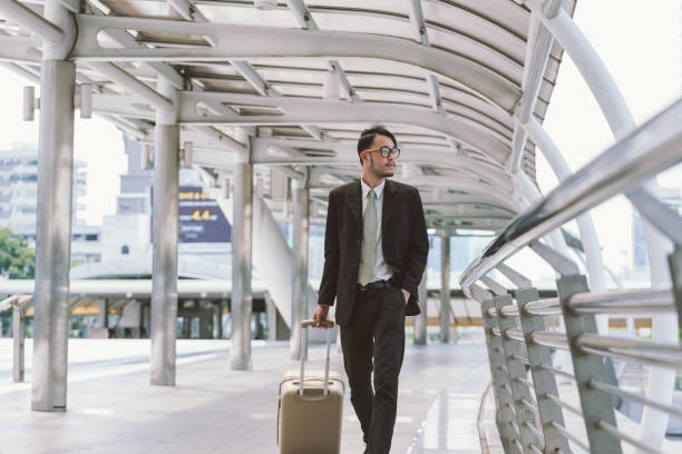 istock Businessman calling on cell phone while pulling baggage and walking in outdoor covered walkway, panoramic banner with copy space 698035406
