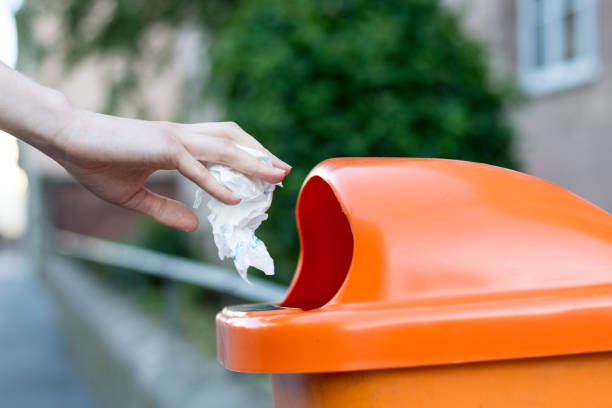 istock Throwing waste into a an orange trash can in the street from the side 698040848