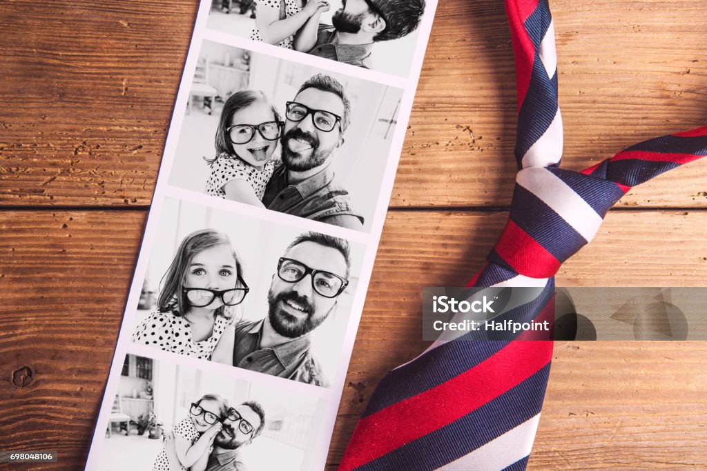 Pictures of father and daughter on table. Fathers day. Studio shot. Colorful tie and various pictures of young father and his cute little daughter. Fathers day concept. Studio shot on wooden background. Father's Day Stock Photo