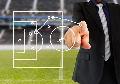 hand of a football coach drawing a tactics of soccer game with white chalk on blackboard at stadium background. All screen content is designed by us and not copyrighted by others and created with digitizing tablet and image editor