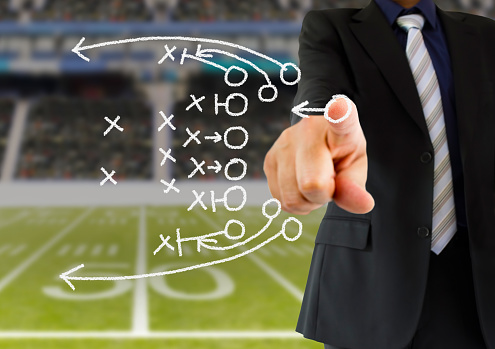 hand of a american football coach drawing a tactics of  football game  with white chalk on blackboard at arena stadium. All screen content is designed by us and not copyrighted by others and created with digitizing tablet and image editor
