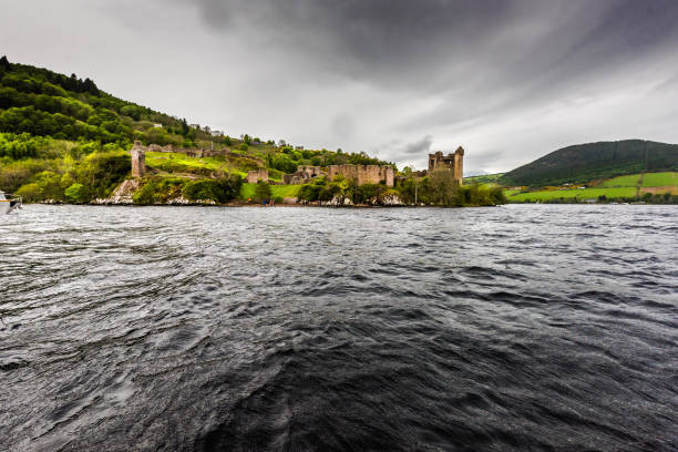 Ruins of Urquhart castle as seen from Loch Ness Ruins of the beautiful Urquhart castle and the hills containing the castle taken during boat ride on the loch ness. The gloomy day and the clouds provide a dramatic effect to the ruins. drumnadrochit stock pictures, royalty-free photos & images