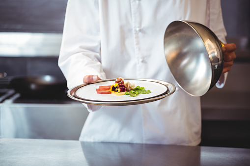 Chef raising a bell of a dish in commercial kitchen