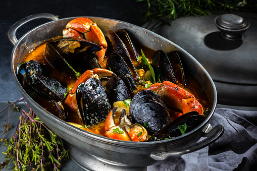 seafood mussels crabs soup in metal pot on gray slate background