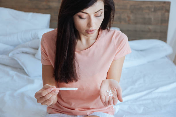 istock Pregnant brunette looking distressingly at pills 698105984