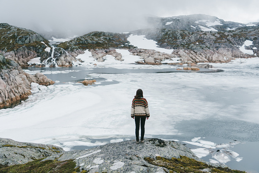 Young Caucasian woman in knitted sweater looking at frozen lake in Norway