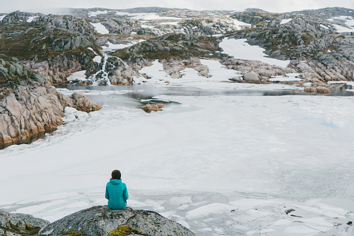 Young Caucasian woman looking at frozen lake in mountains in Norway