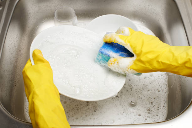 istock Hands in gloves washing plate with blue sponge against sink 698113828