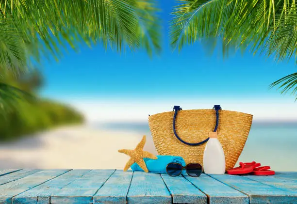 Tropical beach with sunbathing accessories placed on blue wooden planks, summer holiday background. Travel and beach vacation, free space for text.